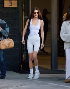 a woman walking down the street in white shorts and tank top with her handbag