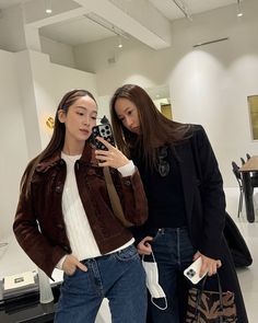 two young women standing next to each other holding cell phones and looking at the camera