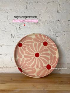 a pink and red plate sitting on top of a wooden table next to a white brick wall