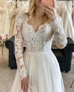 a woman taking a selfie wearing a wedding dress in a bridal shop with her cell phone