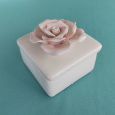 a small white box with a pink flower on the lid sitting on a green surface