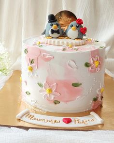 a wedding cake with two birds on top and flowers around the edges, sitting on a table