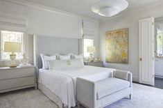 a white bed sitting in a bedroom next to two lamps and a painting on the wall