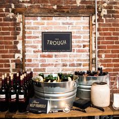 bottles of wine are sitting in buckets on a table next to a brick wall