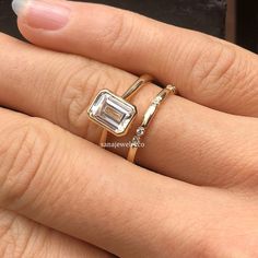 a woman's hand with two gold rings and an engagement ring on her finger