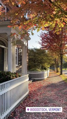 a white house surrounded by trees with fall leaves on the ground and below it is a sign that says woodstock, vermont