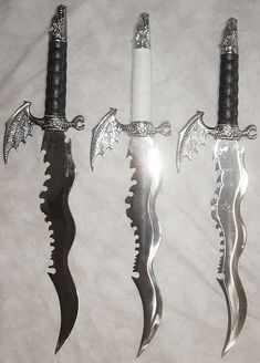 three knives with dragon handles are on a white sheet and one knife has an elaborate handle