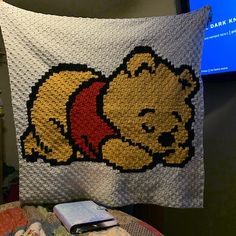 a winnie the pooh crocheted blanket hanging on a wall next to a cell phone