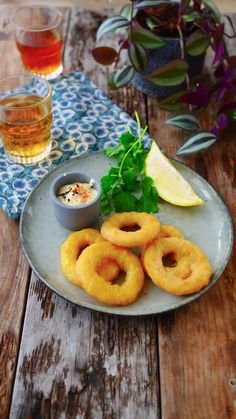 some onion rings are on a plate next to a glass of beer and lemon wedges