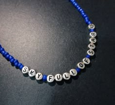 a blue beaded necklace with silver letters and numbers on the beads is laying on a black surface