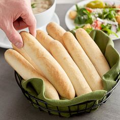 a basket filled with breadsticks sitting on top of a table next to a bowl of salad