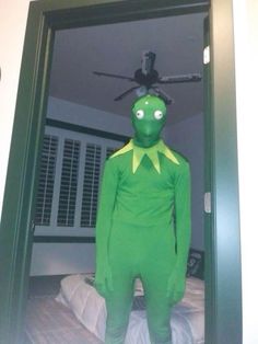 a man in a green frog costume standing in front of a mirror with his eyes open