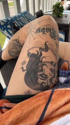 a woman laying on top of a bed next to a chair with tattoos on her legs