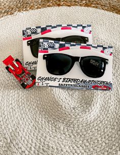 two pairs of sunglasses sitting on top of a white blanket next to a red toy truck