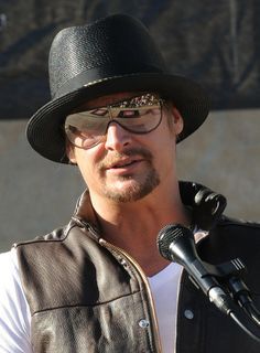 a man wearing a hat and glasses speaking into a microphone