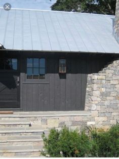 a stone building with a metal roof and two doors on the front door is surrounded by greenery