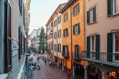 people are walking down the street in an old european city with tall buildings and balconies