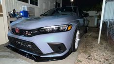 a silver car parked in front of a house with the hood up and lights on