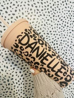 a person holding a coffee cup with the word danielle on it's sleeve, in front of a leopard print wall