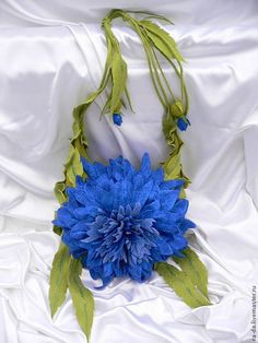 a blue flower is on a white cloth with long green stems and leaves hanging from it's center