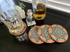 three coasters with blue and gold designs on them next to a bottle of alcohol