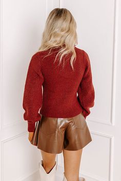 a woman in brown leather shorts and a red sweater is looking down at the wall