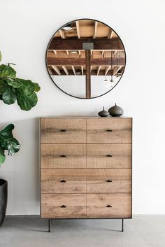 a wooden dresser sitting next to a potted plant in front of a round mirror