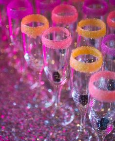 many wine glasses are lined up on a table with pink and purple sequins