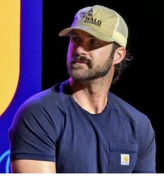 a man wearing a hat and looking off to the side while standing in front of a sign