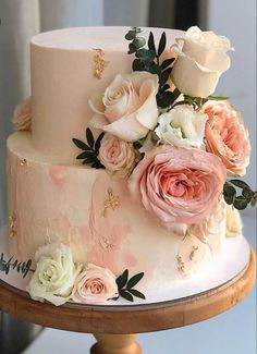 a three tiered wedding cake with pink and white flowers on the top, sitting on a wooden stand