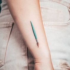 a woman's arm with a small green pen tattoo on the left forearm and wrist