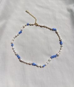 a blue and white beaded necklace on a white sheet with a gold plated clasp