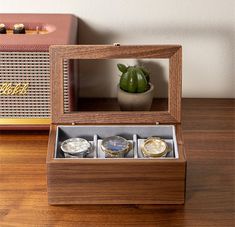 three watches in a wooden box on a table next to a radio and a cactus