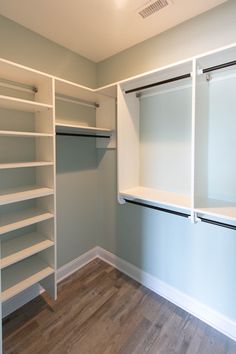 an empty walk in closet with white shelving and wood flooring on the side