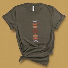 This terra-cotta moon phases graphic tee was Inspired by the beacon of light that illuminates the night sky, our majestic moon. The rustic boho shapes of the moon and clay color harken to the warm hues of the south western desert. Celebrate all the phases of life, and love with this simple and elegant clay moon phase shirt. DETAILS This Beautiful graphic t-shirt is made of 49% to 100% combed and ring-spun cotton and is very soft and comfortable to wear. Check the size card for specific fabricati Graphic Tee Shirt With Moon Print, Relaxed Fit Graphic Tee With Moon Print, Relaxed Fit Moon Print Graphic Tee, Cotton Crew Neck Tops With Sun And Moon Design, Cotton Tops With Sun And Moon Design, Relaxed Fit, Full Moon Shirt, Boho Shapes, Clay Moon, Moon Phases Shirt