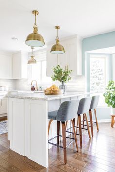 a kitchen island with four stools in front of it and two hanging lights above it