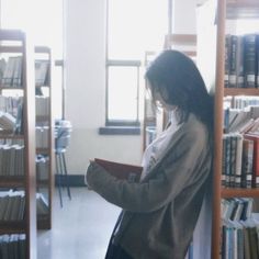 a woman standing in front of a bookshelf holding a book