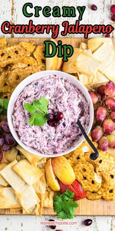 a bowl of dip surrounded by crackers and fruit on a cutting board with the words creamy cranberry jalapeno dip