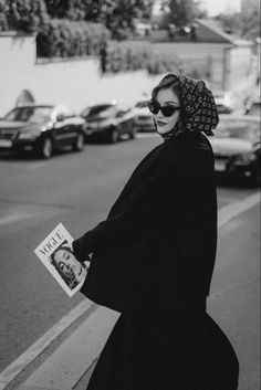 a woman walking down the street while wearing a scarf on her head and reading a book