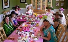 a group of women sitting at a table with plates and cups on it, all dressed in fancy hats