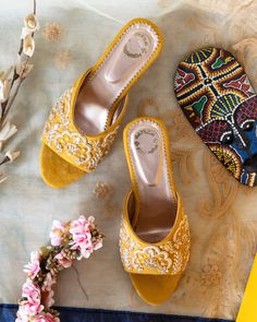 two pairs of yellow shoes sitting on top of a blue and white blanket next to flowers