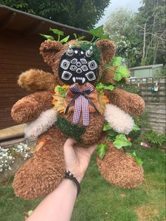 a person holding a teddy bear with leaves on it's face and wearing a mask