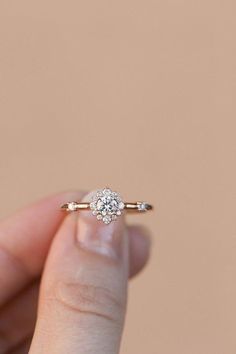 a woman's hand holding an engagement ring in front of a beige background,