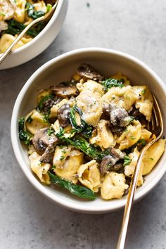 two bowls filled with pasta and spinach covered in mushrooms, parmesan cheese and herbs