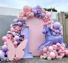 a pink and purple balloon arch with a blue horse on the number one surrounded by balloons