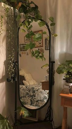 a mirror sitting on top of a wooden table next to a plant filled wall in a room