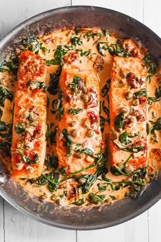 fish covered in sauce and spinach leaves on a metal pan with white wood background