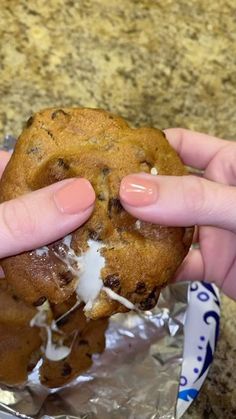 a person holding a chocolate chip cookie in their left hand, on top of aluminum foil