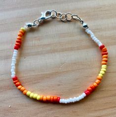 A Silver, adjustable bracelet made from white, red, orange, and yellow seed beads in a gradient pattern. Adjustable Orange Friendship Bracelets With Colorful Beads, Adjustable Orange Beaded Bracelets, Adjustable Orange Heishi Bead Bracelet, Orange Beaded Heishi Bracelets, Adjustable Orange Jewelry With Letter Beads, Casual Orange Beaded Jewelry, Adjustable Orange Beaded Bracelet With Tiny Beads, Adjustable Orange Beaded Bracelets With Tiny Beads, White Beaded Adjustable Friendship Bracelets