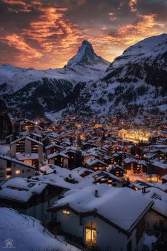 the sun is setting over a small town with mountains in the background and snow on the ground